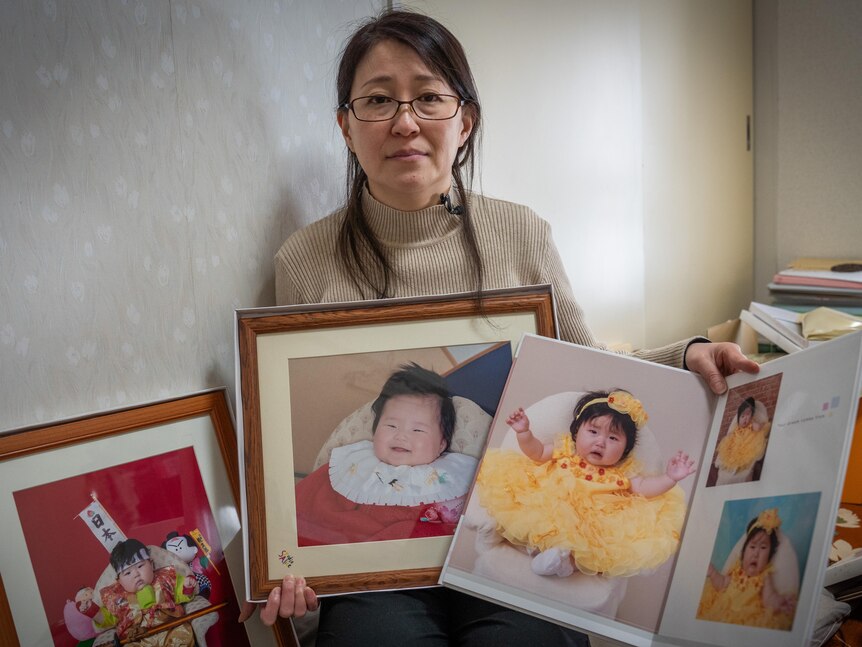 A woman holding photos of her three children.