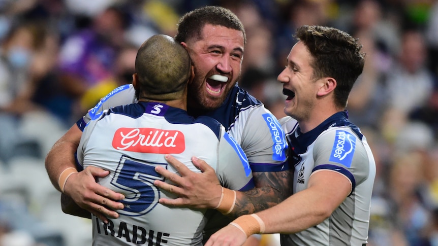 Three Melbourne Storm NRL players embrace as they celebrate a try.