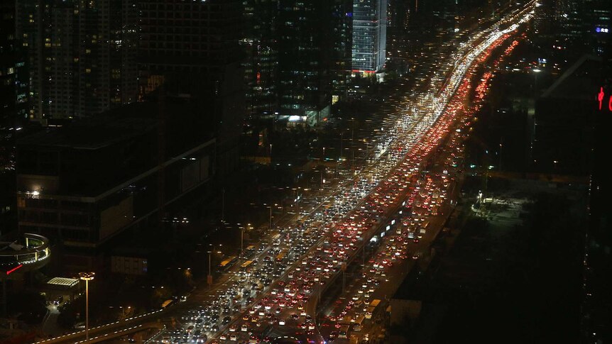 A very long traffic jam on a multi-lane highway through a large city.