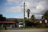 A power pole and two houses next to it in suburban Perth. Partly cloudy sky in the background.