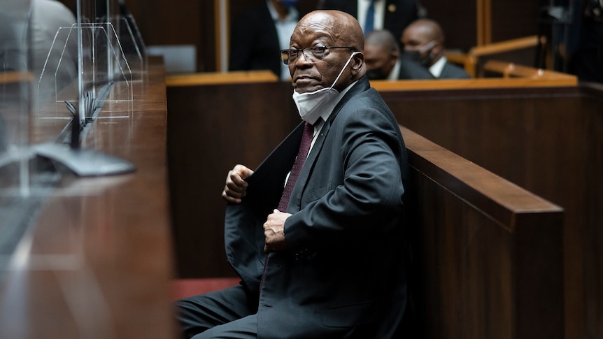 A side shot of Mr Zuma sitting down in court looking at the camera. 