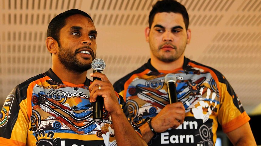 Preston Campbell holds a microphone standing in front of Greg Inglis
