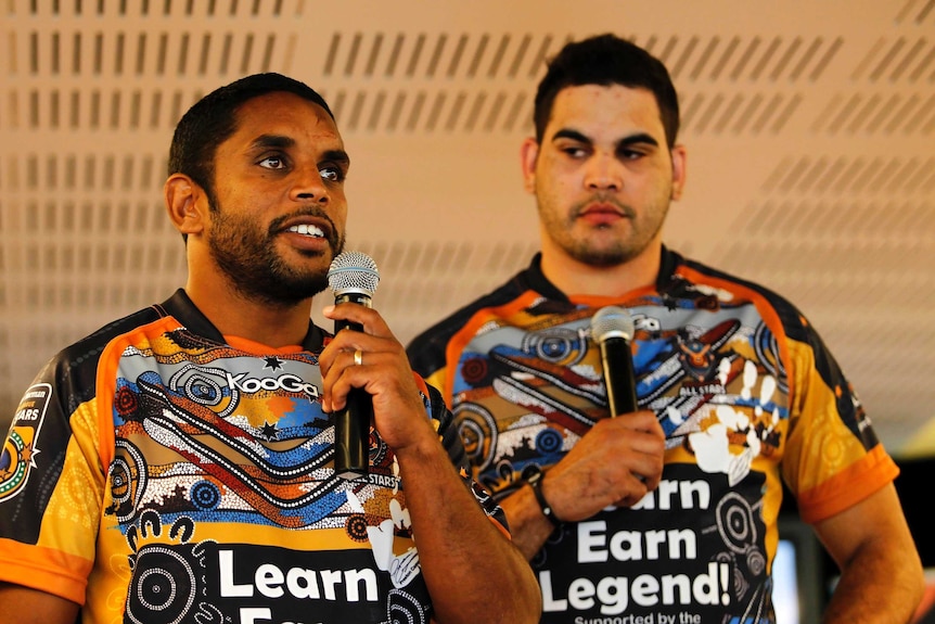 Preston Campbell holds a microphone standing in front of Greg Inglis