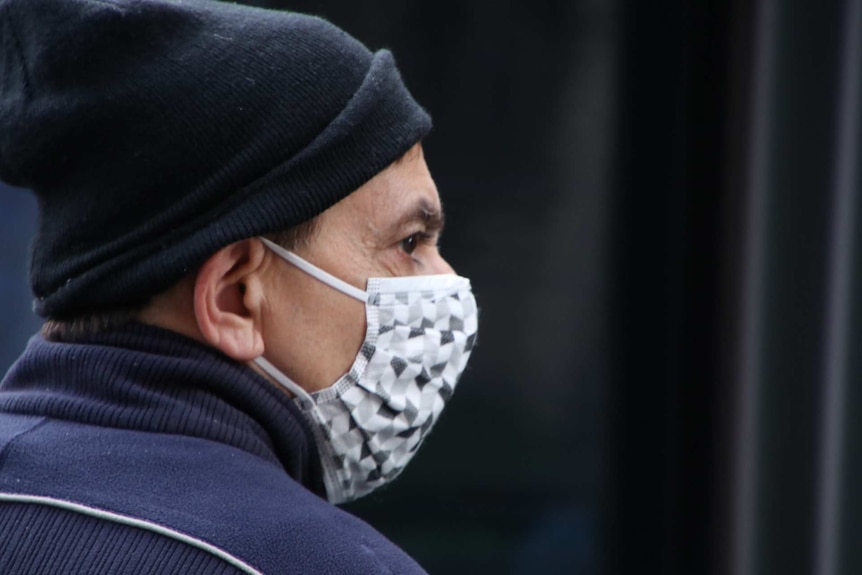 A side-on shot of a man in a beanie wearing a cloth mask