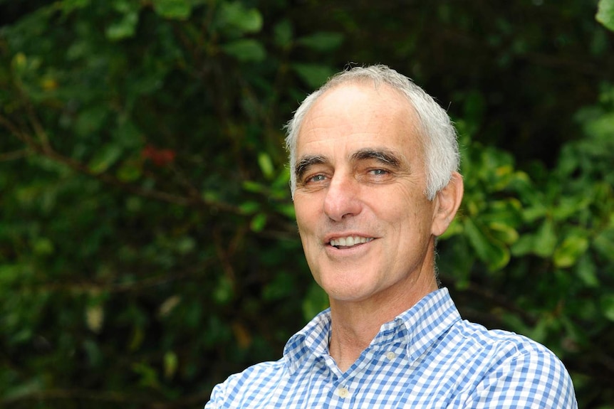 A man stands smiling in a macadamia orchard.