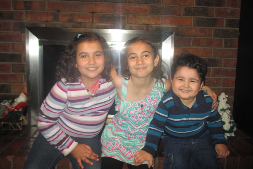 Two little girls sit next to a smiling boy