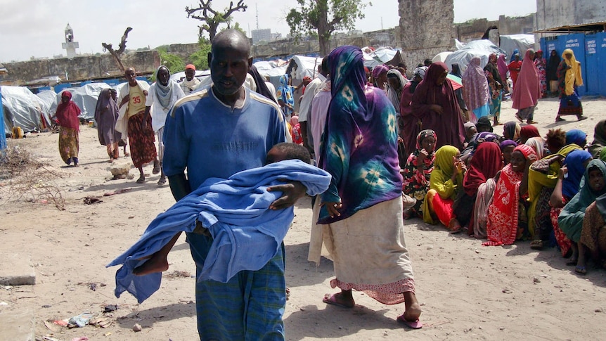 An internally displaced Somali man carries his malnourished child to a health facility at a camp in Mogadishu.