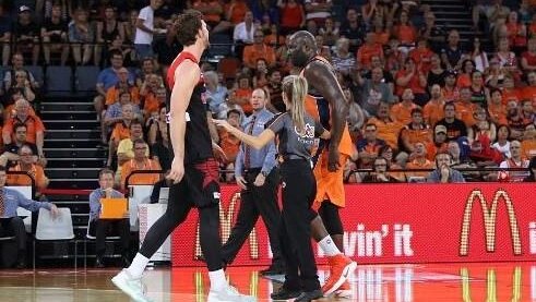 Two tall basketball players tower on each side of referee Toni Caldwell as the audience watches the game from the sidelines.