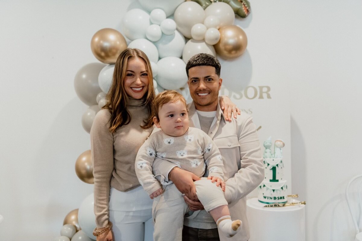 A mum and dad hold their baby and smile for the camera at a first birthday