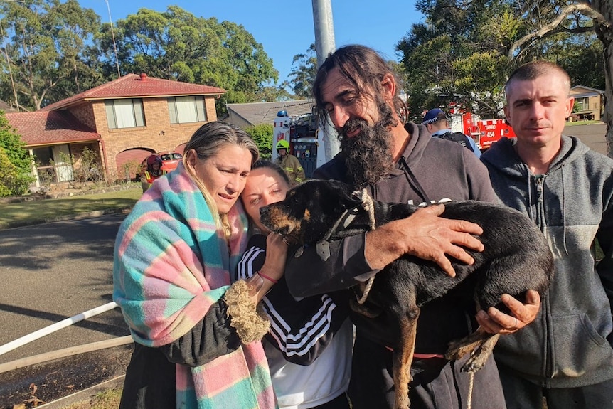 Two men and two women hold a black dog in their arms in a suburban street.