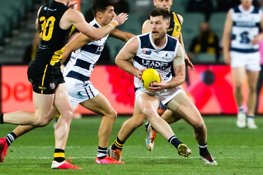 A football player crouches with a yellow ball while surrounded by other players.