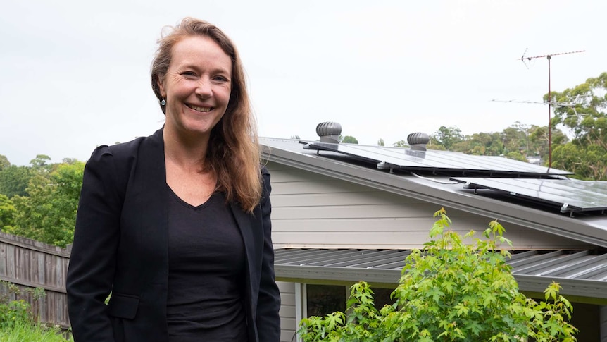 Kate Friend standing in her garden with solar panels on her roof behind her