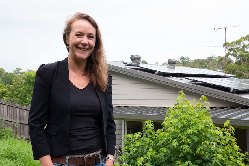 Kate Friend standing in her garden with solar panels on her roof behind her