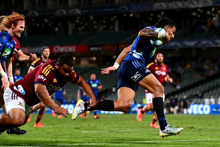 A Super Rugby player maintains his balance heading for the tryline as a defender tries to ankle=tap him.