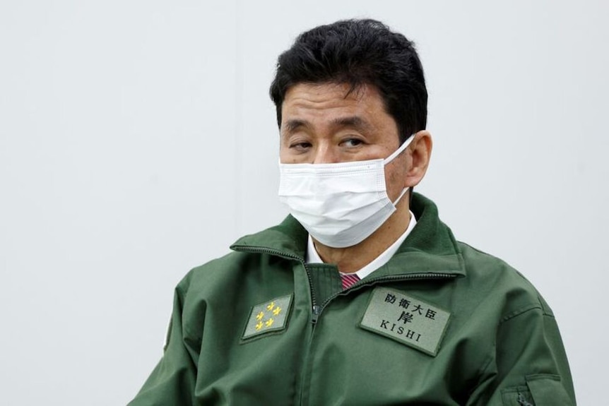 Japan's Defense Minister Nobuo Kishi wearing a green top and protective mask.