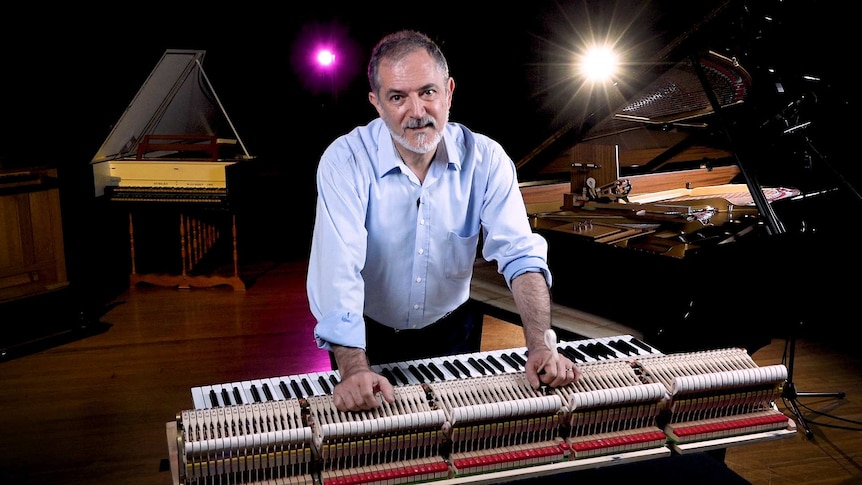 Ara Vartoukian with his sleeves rolled up leaning on the keyboard mechanism of a grand piano.