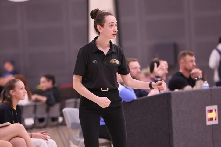 A woman basketball coach is standing on the sidelines, watching a game.