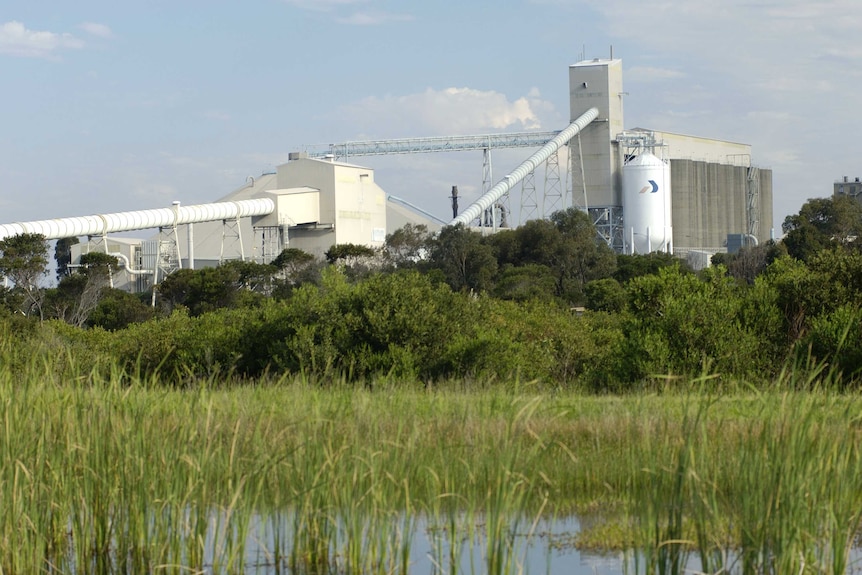 A factory with a pond and green grass in the foreground.