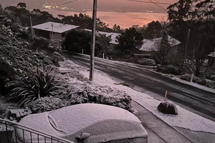 A view down on to a car and nature strip covered in snow in the early morning