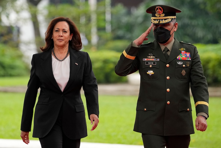 Ms Harris walking next to a guard who is saluting. 