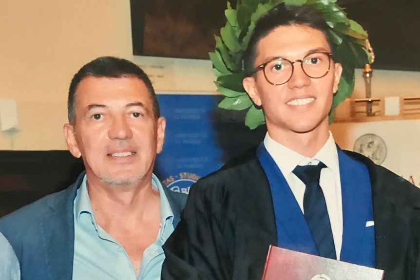 A father and son pictured at a graduation, with the son in robes.