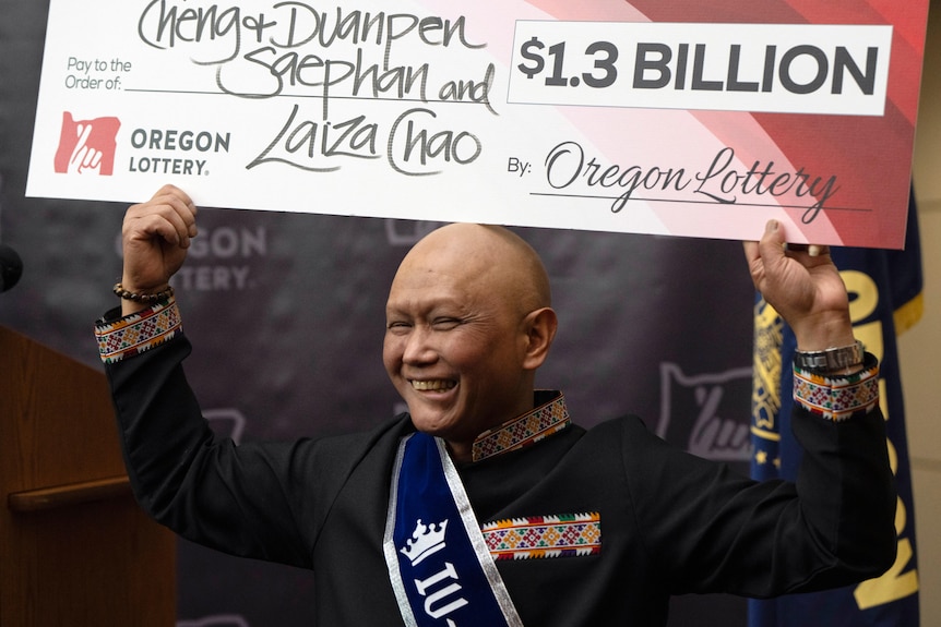 A bald man holds a giant cheque for $1.3 billion above his head.