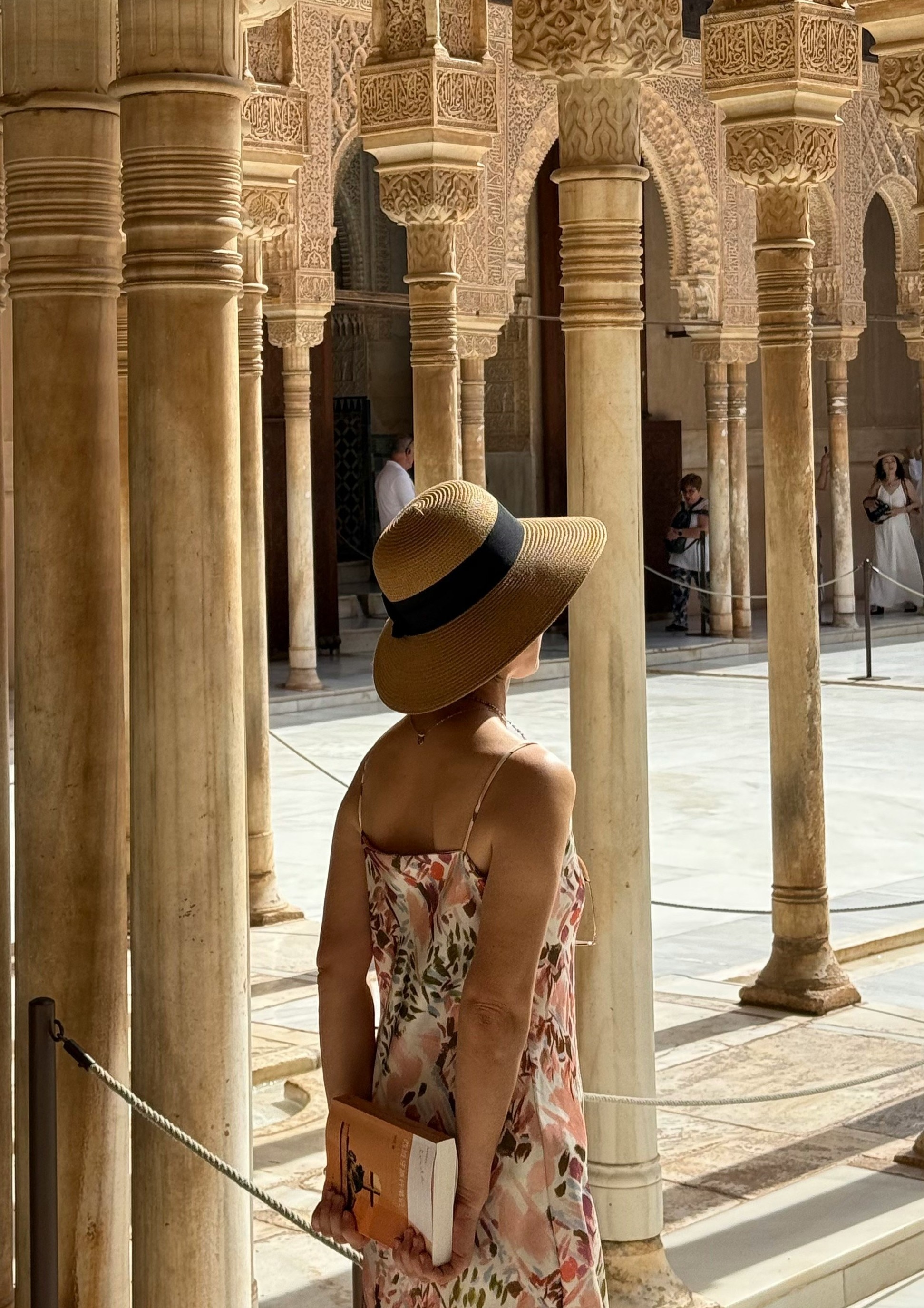 A Woman in a sundress stands among stone pillars at Spanish tourism site. Her faces is hidden by a straw hat.