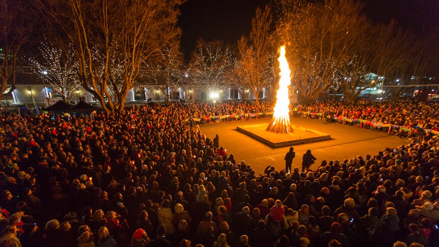 A large bonfire in a square surrounded by people in the dark