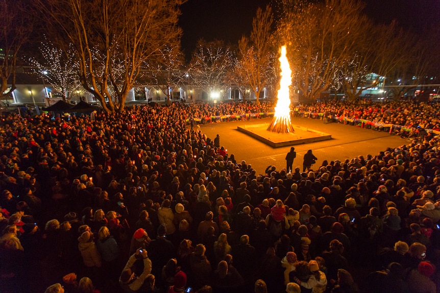 A large bonfire in a square surrounded by people in the dark