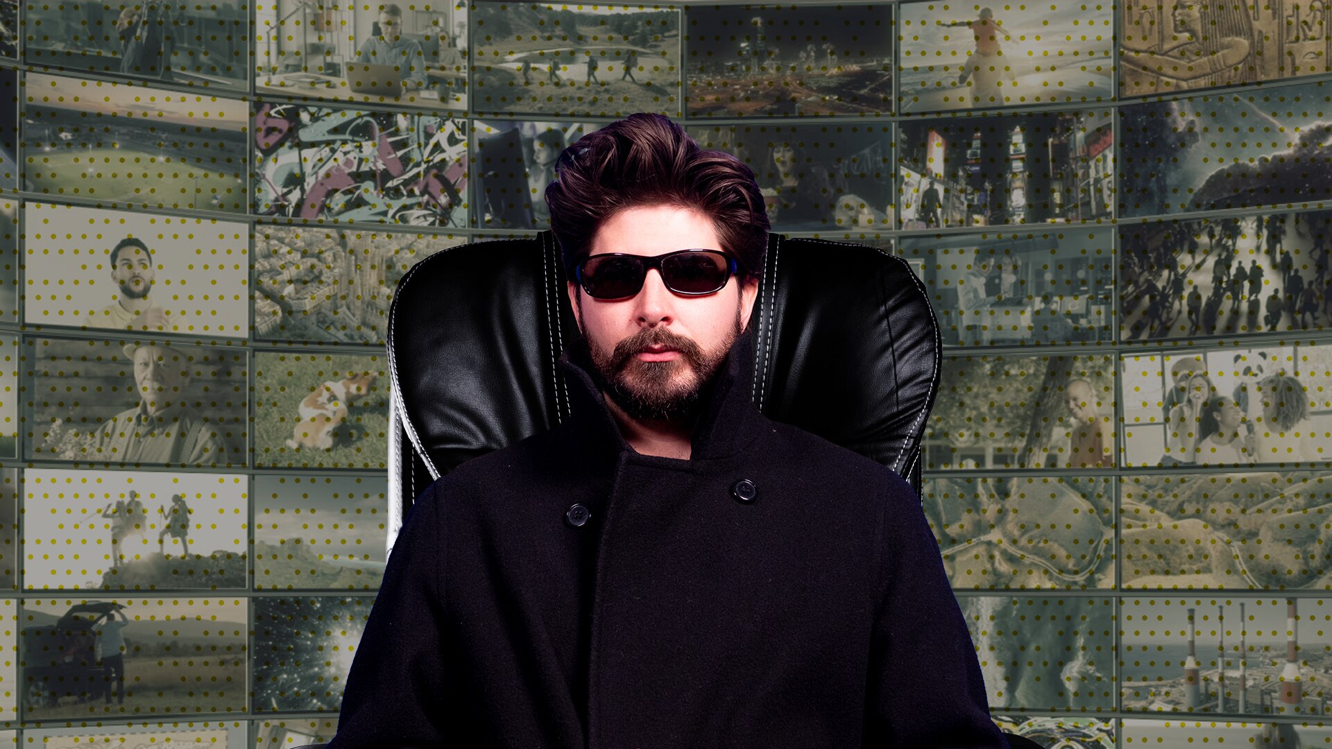 Joe dressed in black with dark sunglasses on looks serious while sitting on a high back chair. A wall of screens behind him.