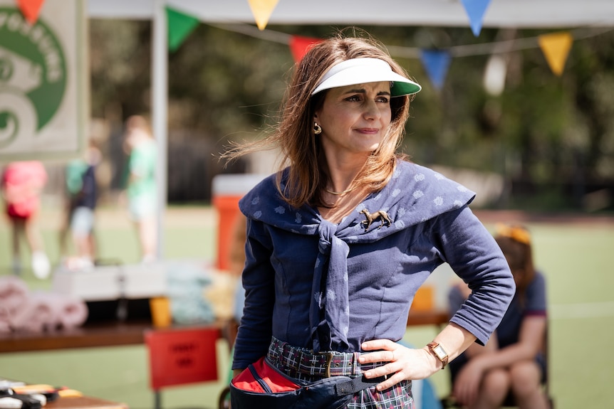 Pia Miranda wears a visor on a sunny day, looking concerned with hand on hip. Blurred in the background, a school athletics day.