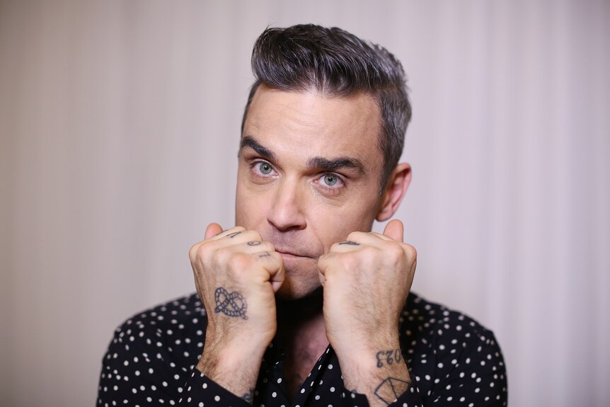 Singer Robbie Williams raises his hands in front of the lower half of his face as he poses for a photo inside a studio in Sydney