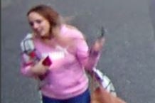 CCTV footage of a young woman with blonde hair, wearing a pink jumper and blue jeans carrying a phone and large brown handbag.