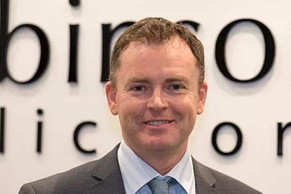 man in tie and jacket looking at camera with part of sign in background