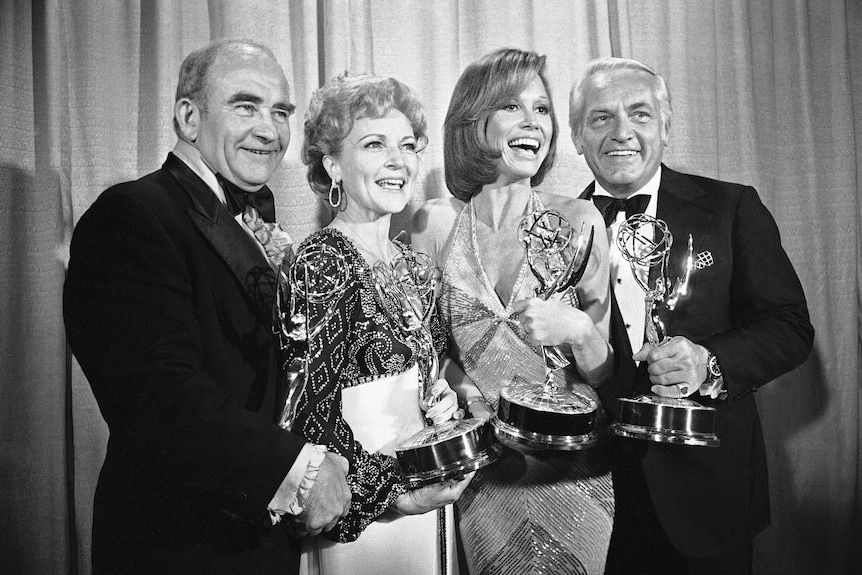 Four people stand holding Emmy trophies 