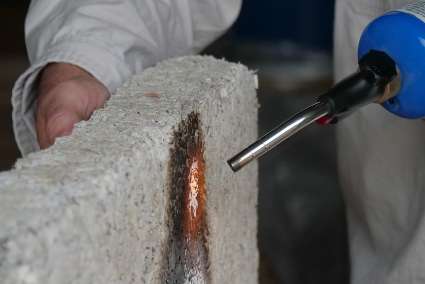 A small section of a grey hemp brick glows red from the flame of a blow torch.