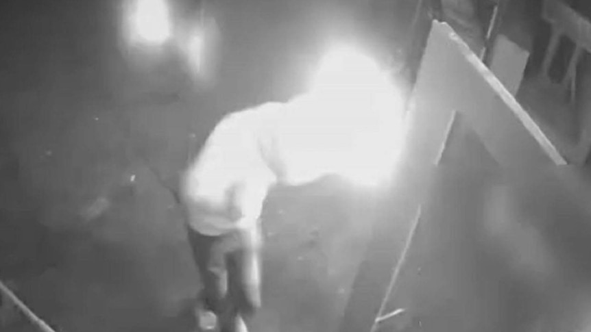 Black and white CCTV of a man setting his sleeve on fire after breaking into a cafe.