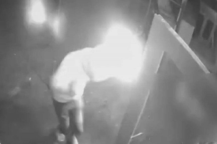 Black and white CCTV of a man setting his sleeve on fire after breaking into a cafe.