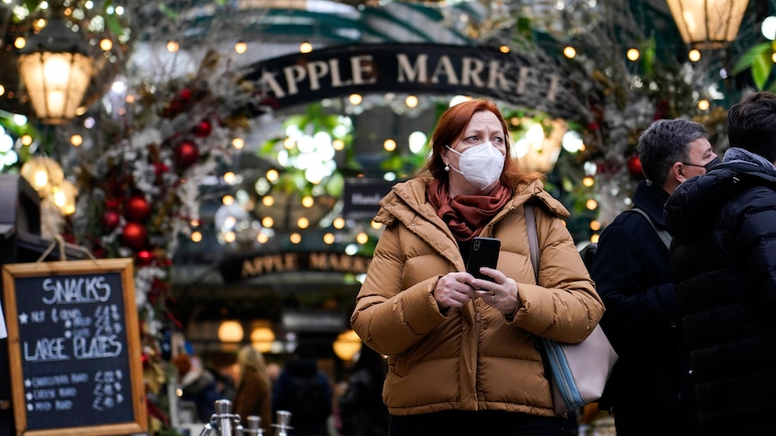 Una donna che indossa un cappotto oversize e una maschera per il viso mentre cammina attraverso il mercato di Covent Garden