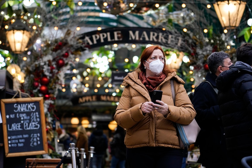 A woman wearing a big coat and a face mask as she walks in Covent Garden market