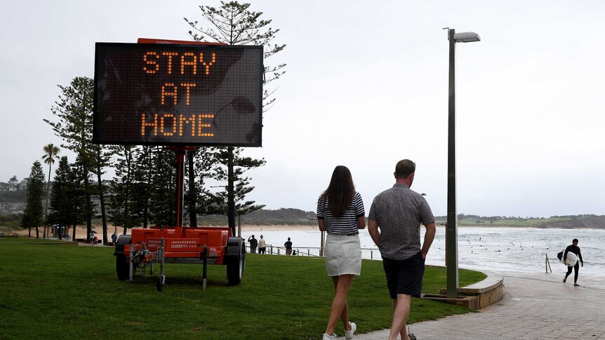 People walk past a sign saying "Stay at home".
