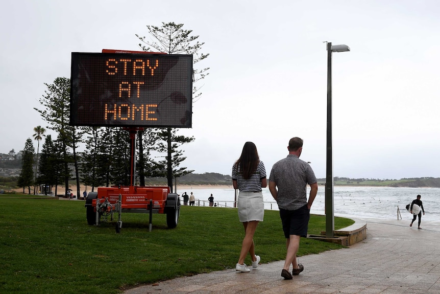 People walk past a sign saying "Stay at home".