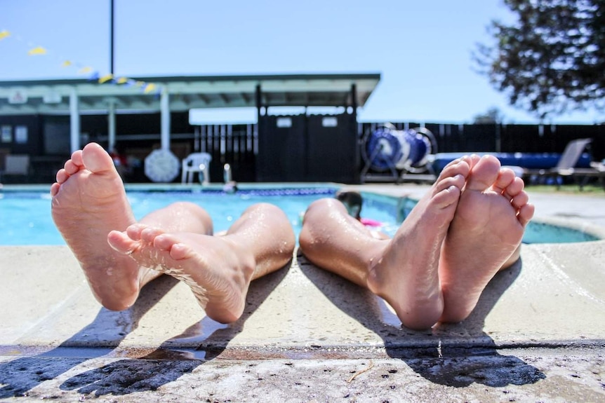 two sets of feet sticking up out of a sunny pool