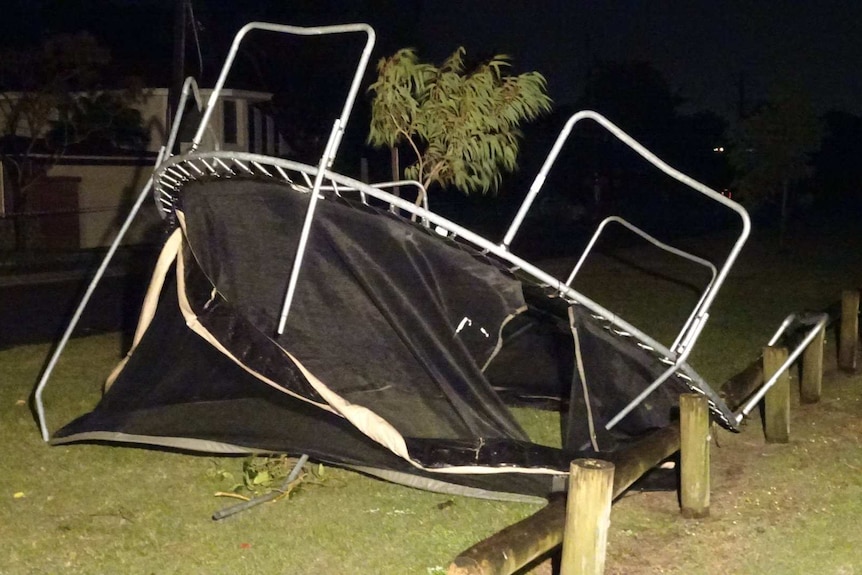 A trampoline lies crumpled and upside down at the side of a park.
