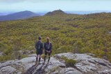 Two people standing on top of a hill overlooking a Tasmanian forest