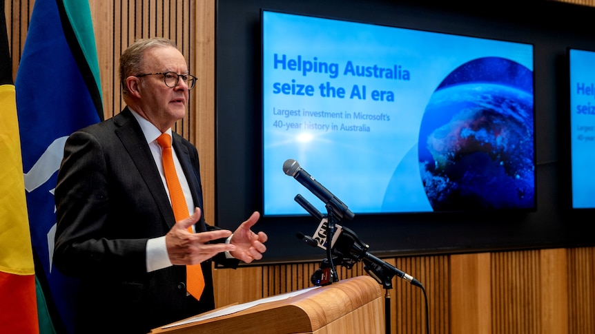 Anthony Albanese stands next to a screen that says "helping Australia seize the AI era".