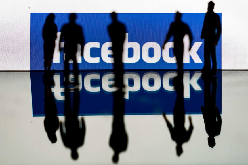 Five people are silhouetted against a screen showing the Facebook logo. Their shadows and the logo are reflected on the floor.