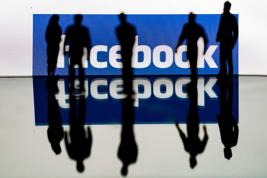 Five people are silhouetted against a screen showing the Facebook logo. Their shadows and the logo are reflected on the floor.