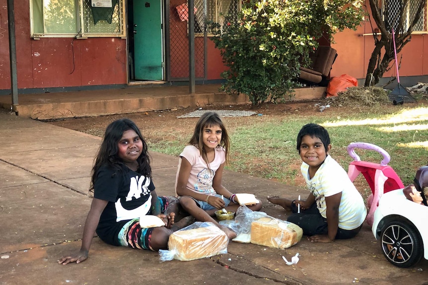 Three Aboriginal kids sitting in driveway with food in Broome