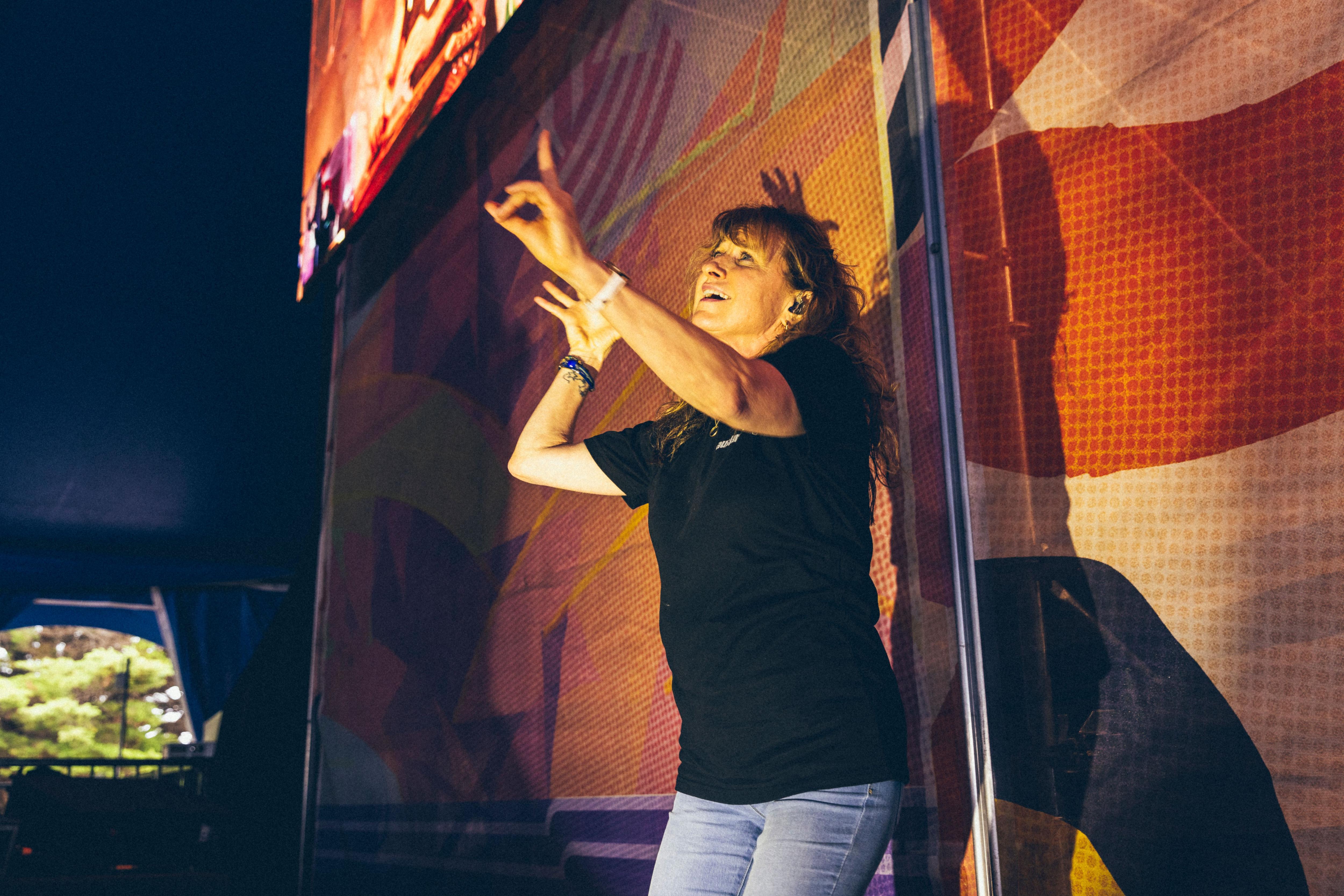 A woman signing Auslan in front of a colourful flag with a lit up stage in the distance